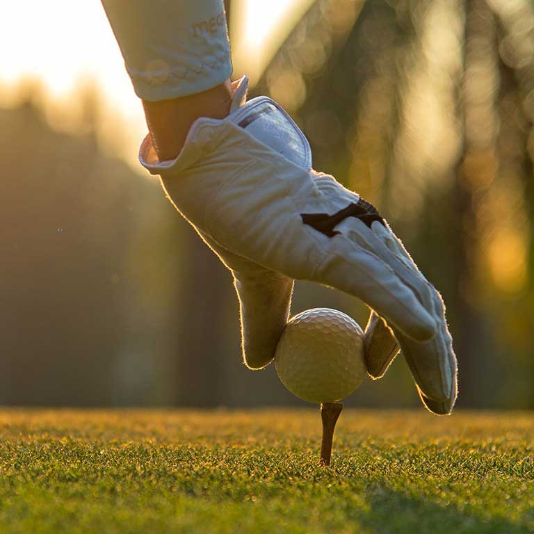 Golfer putting golf ball on tee in golf course.